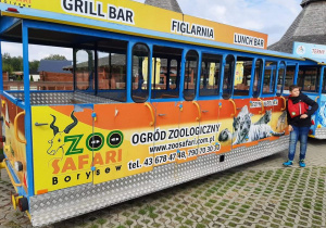 Chłopiec opiera się o pomarańczowy wagon restauracyjny z napisem ZOO Safari Borysew.