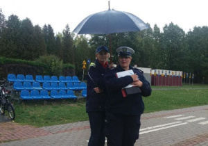 Policjantka wraz z nauczycielką obserwują jadącego na rowerze ucznia.