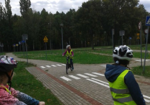 Uczniowie obserwują jadącą na rowerze koleżankę.