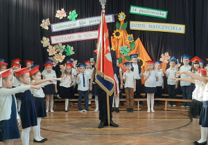 Uczniowie stoją z podniesionymi rękami do ślubowania, na środku stoją uczniowie starszych klas ze sztandarem szkolnym.