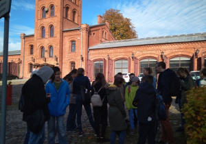 Grupa uczniów wraz z przewodnikiem przez dawnym budynkiem straży pożarnej przy ul. Tymienieckiego