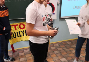 Uśmiechnięty uczeń z naszej szkoły wręcza koleżance dyplom i nagrodę za wygrany konkurs.