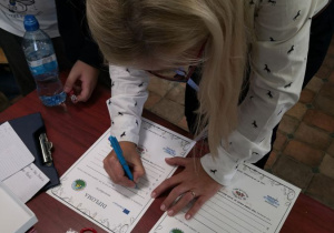 Koordynator projektu Erasmus+ wypełnia dyplomy dla uczniów biorących udział quizie na temat przeciwdziałania przemocy w szkole.