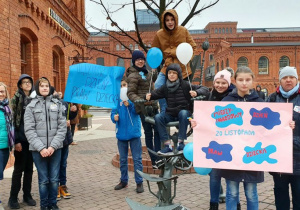 Grupa uczniów wraz z koordynatorkami pokazuje w zbliżeniu napisy na plakatach: 20 listopada Międzynarodowy Dzień Praw Dziecka.