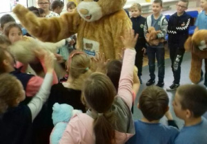 Miś Teddy Eddi stoi w środku koła i przybija piątki na powitanie z uczniami.