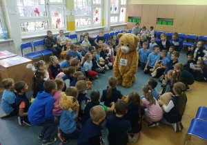 Miś Teddy Eddi siedzi na środku koła i opowiada ciekawe historie uczniom siedzącym w kole.