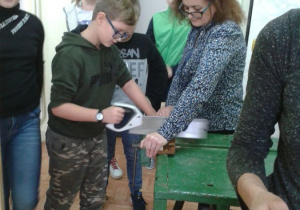 Uczeń przeżyna kawałek drewna, nauczyciel asekuruje go.