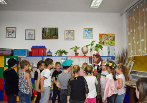 Dzieci stoją w kręgu i słuchają co mówi nauczycielka ubrana w strój ludowy.