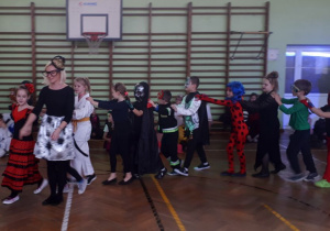 Nauczycielka w przebraniu prowadzi korowód licznej grupy dzieci będących w przebraniach.