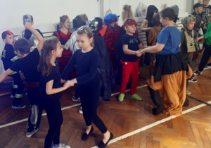 Liczna grupa dzieci w przebraniach stoi w parach, trzymając się za obie ręce.