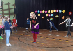 Nauczyciel w przebraniu pokazuje gesty rękami, dookoła grupa dzieci naśladuje te gesty.