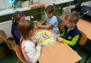Trzy dziewczynki i jeden chłopiec siedzą przy wspólnym stoliku i grają w grę planszową.
