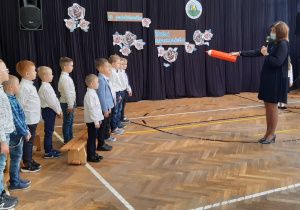 Pani dyrektor symbolicznym ołówkiem pasuje chłopców na uczniów klasy I b.
