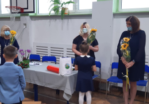 Uczniowie wręczają kwiaty nauczycielom z okazji Dnia Edukacji Narodowej.