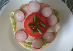 Kanapka – kwiatek. Na pieczywie liść sałaty, plaster wędliny, rzodkiewka, pomidor ozdobiony szczypiorkiem
