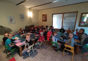Dzieci siedzą przy stolikach na których leżą prace wykonane z papieru czerpanego