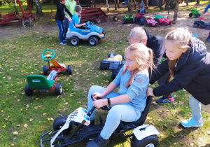 Dziewczynka siedzi na quadzie, którego pchają inne dzieci