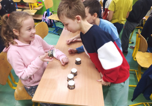 Dziewczynka w różowej bluzie pokazuje koledze w kolorowej bluzie, co wylosował.