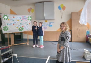 Ddwie dziewczynki stoją na scenie z mikrofonem w ręku i śpiewają kolędę. Przed sceną stoi Pani prowadząca konkurs.