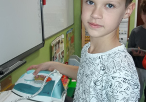 Uczeń prasuje żelazkiem kartkę, pod którą jest kalka techniczna i liść.
