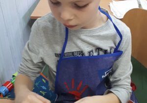 Chłopiec ubrany w fartuszek obiera jajko ze skorupki.
