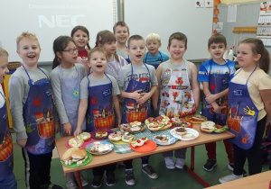 Grupa rozbawionych dzieci prezentuje przygotowane kanapki.
