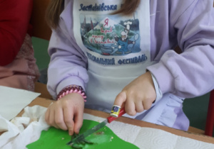Dziewczynka kroi na deseczce składniki na kanapkę.