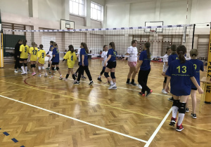 Drużyna dziewcząt, ustawiona wzdłuż siatki dziękuje za mecz innej drużynie.