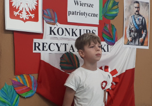 Uczeń na tle tablicy z napisem "Konkurs recytatorski - wiersze patriotyczne"