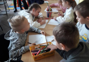 Dzieci siedzą przy stolikach i kolorują ilustrację ptaka