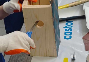 Przyklejanie tapety do ścianki budki, wycinanie otworu.