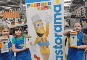 Grupa uczennic na tle plakatu Majsterkowa prezentuje swoje prace.