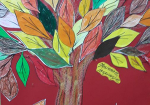 Drzewo z liśćmi w jesiennych kolorach – praca plastyczna na czerwonym tle.