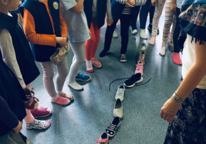 Grupa dziewczynek stoi wokół ustawionych na podłodze - jeden za drugim - butów.