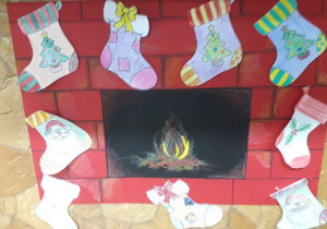 Plakat rysunkowy i wyklejany kominka ze świątecznymi pokolorowanymi skarpetami.