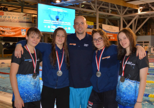 Maja na pływalni, po zawodach, z trenerem i 3 koleżankami z medalami na szyi.