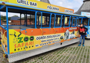 Chłopiec opiera się o pomarańczowy wagon restauracyjny z napisem ZOO Safari Borysew.