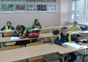 Kilku chłopców ubranych w kamizelki odblaskowe siedząc w ławkach w klasie na Motodromie pisze egzamin teoretyczny na kartę rowerową.