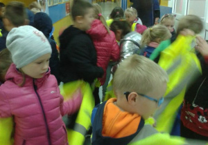 Grupa uczniów zakładająca kamizelki odblaskowe na szkolnym korytarzu.