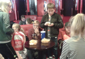 Dzieci siedzą przy stoliku i jedzą popcorn.