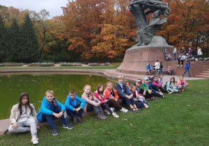 Grupa dzieci odpoczywających nad stawem na tle Pomnika Fryderyka Chopina w Łazienkach.