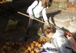 Uczennice sprzątają liście z nagrobków.