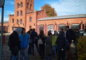 Grupa uczniów wraz z przewodnikiem przez dawnym budynkiem straży pożarnej przy ul. Tymienieckiego