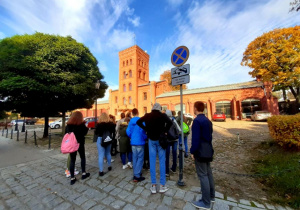 Grupa uczniów wraz z przewodnikiem przez dawnym budynkiem straży pożarnej przy ul. Tymienieckiego