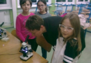 Trzy uczennice pokazują mamie preparat pod mikroskopem.