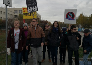 Grupa uczniów trzymających transparenty wraz z opiekunem idą ulicą.