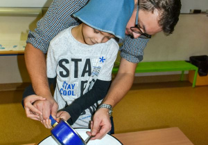 Tata pomaga chłopcu przelewć przez dziurkę od klucza wosk do miski z wodą.