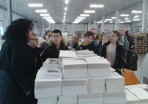 Stos wydrukowanych stron książek, w tle uczestnicy wycieczki, uczniowie klasy VI c.