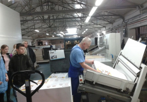 Pracownik drukarni obsługuje maszynę, w tle dzieci.