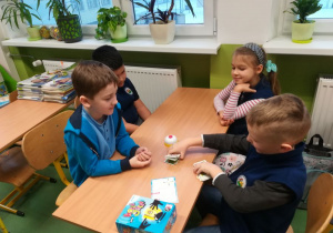 Trzech chłopców i jedna dziewczynka siedzą przy wspólnym stoliku i grają w karty.